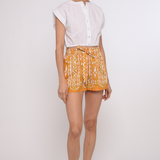 Model wearing tailored tan shorts and white cotton top with a clean, relaxed silhouette.