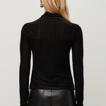 A woman viewed from the back wearing a black long-sleeve mock-neck top with a fine houndstooth pattern, paired with black leather pants, against a light gray studio background.