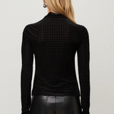 A woman viewed from the back wearing a black long-sleeve mock-neck top with a fine houndstooth pattern, paired with black leather pants, against a light gray studio background.