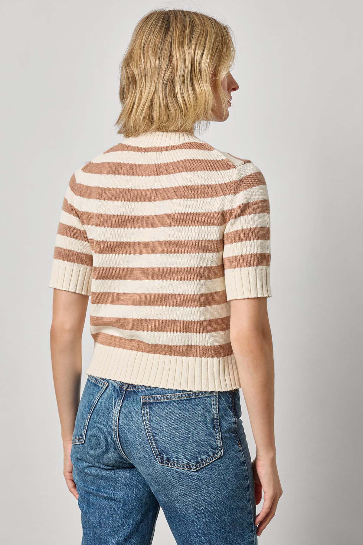 Person wearing a striped sweater and jeans on a plain background
