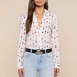 Woman wearing a white blouse with red and black pattern and light blue jeans on a beige background