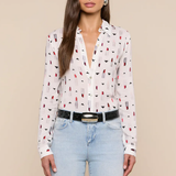 Woman wearing a white blouse with red and black pattern and light blue jeans on a beige background