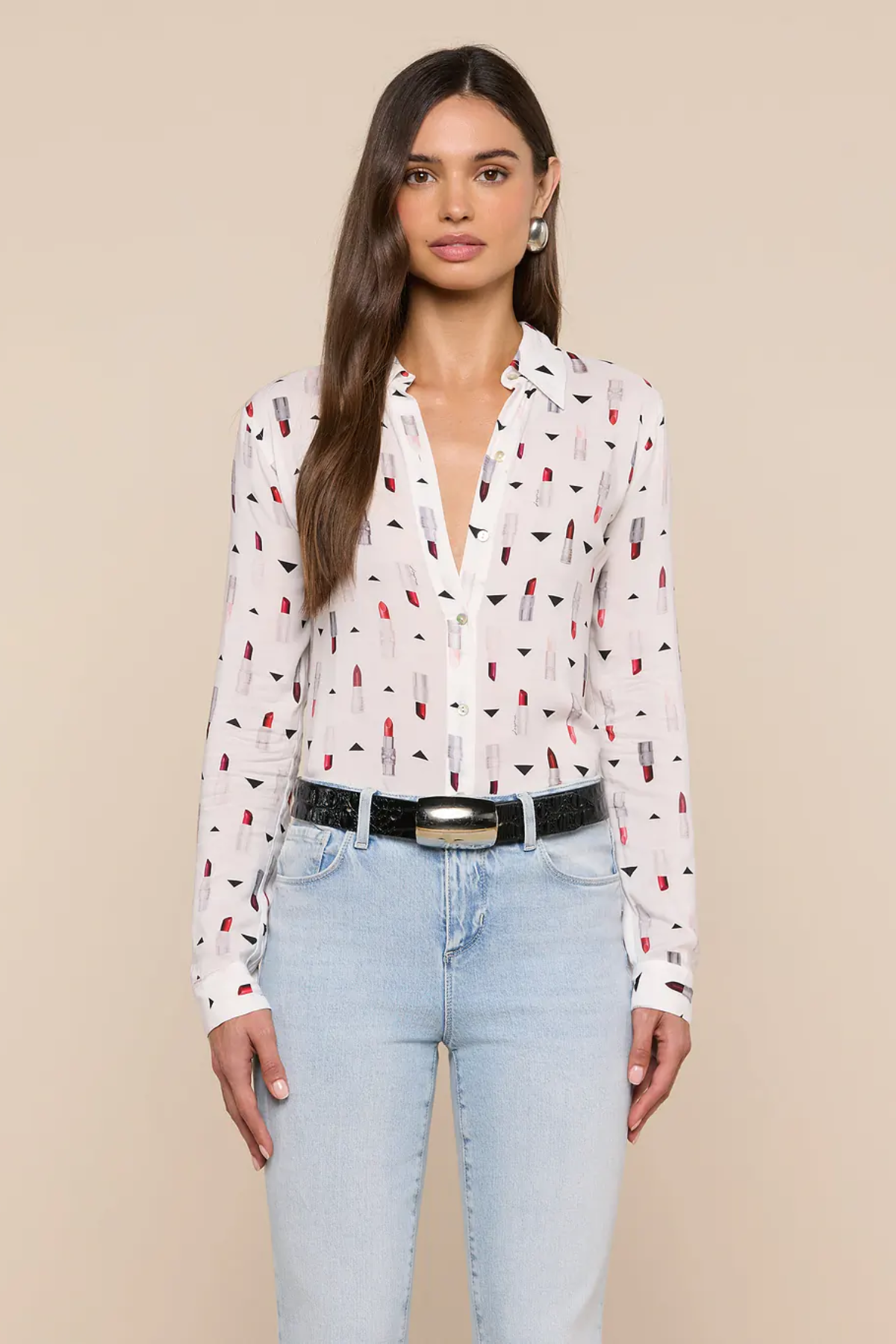Woman wearing a white blouse with red and black pattern and light blue jeans on a beige background