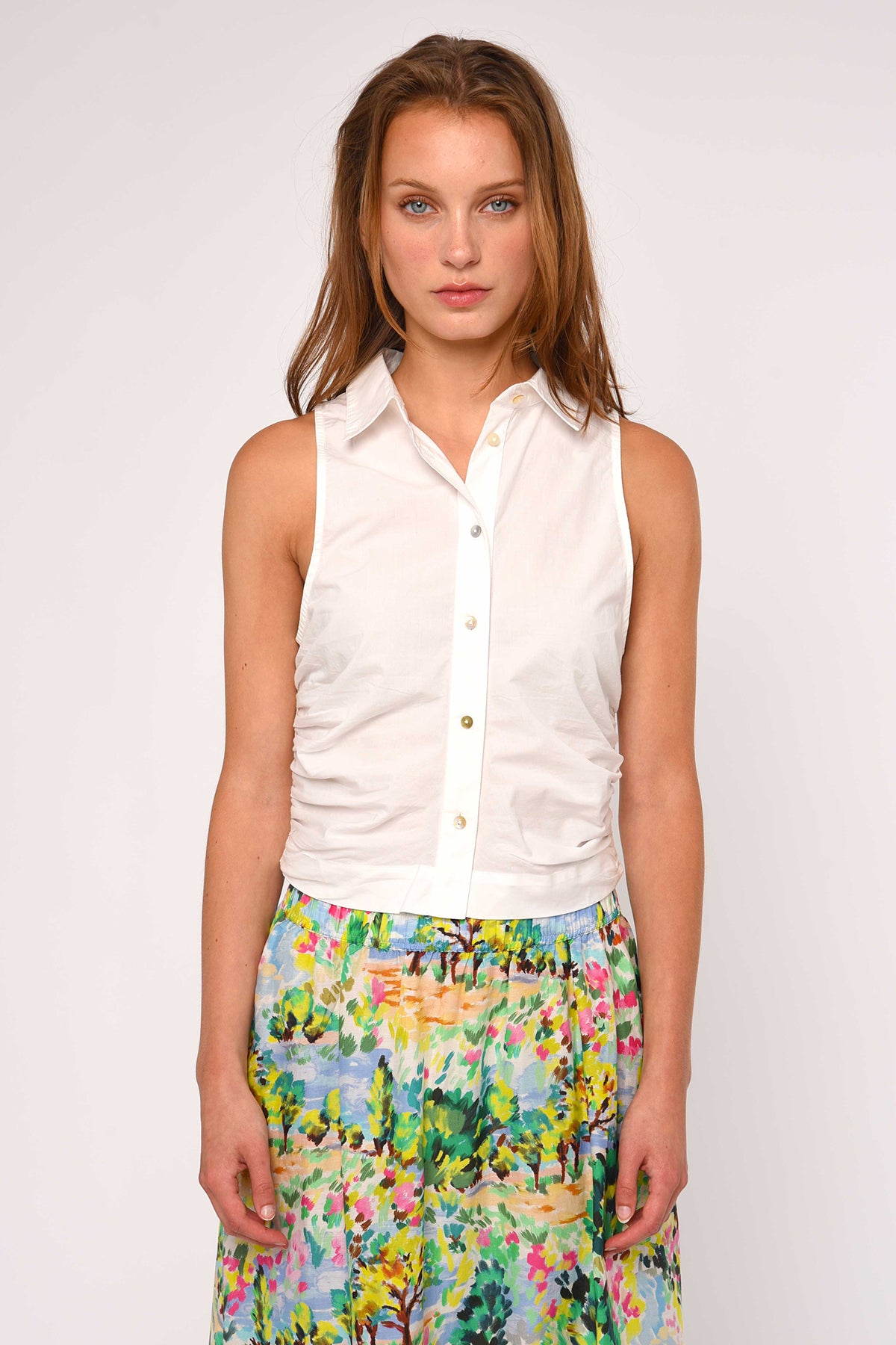 Woman wearing a white sleeveless shirt and colorful floral skirt on a white background