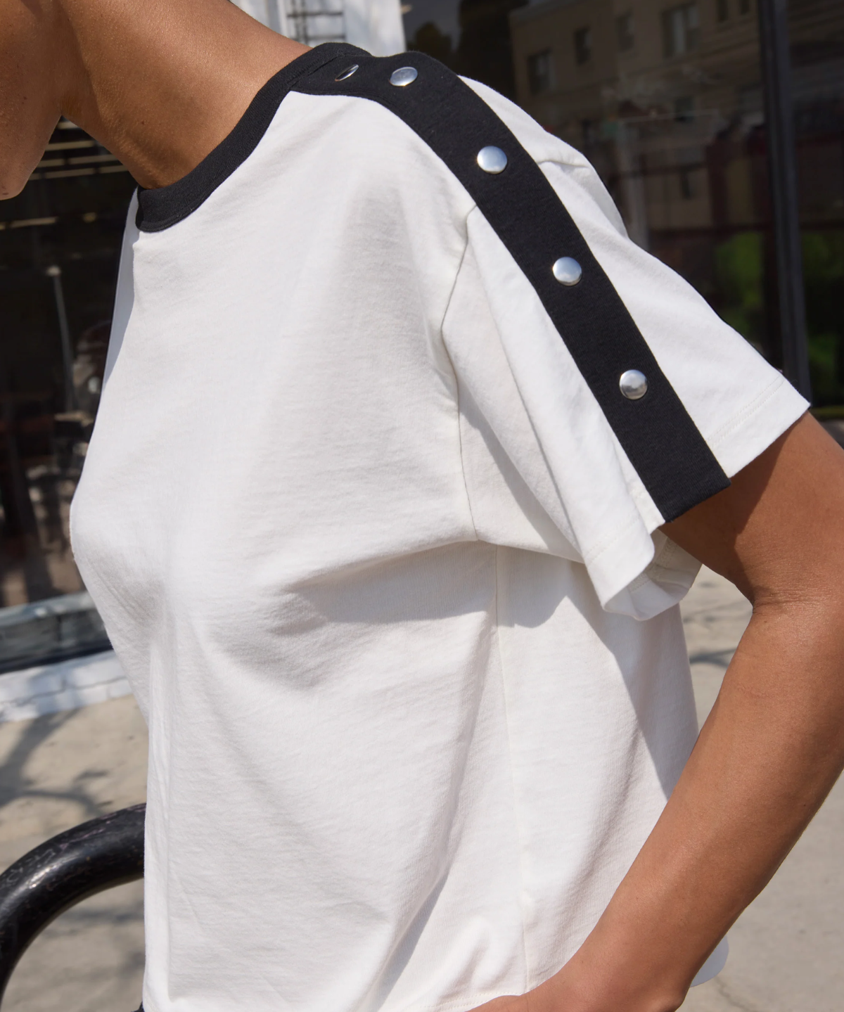 White t-shirt with black trim and silver buttons worn by a person outdoors.