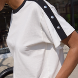 White t-shirt with black trim and silver buttons worn by a person outdoors.