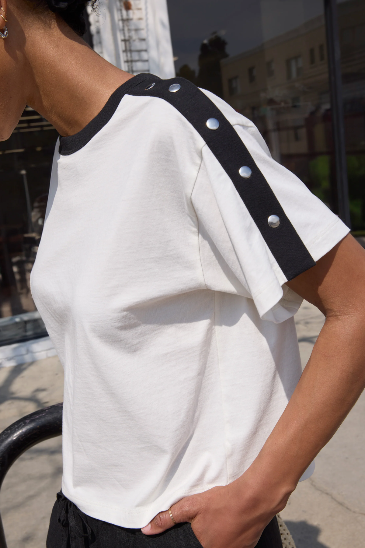 White t-shirt with black trim and silver buttons worn by a person outdoors.