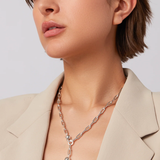 Woman wearing a silver necklace with a heart pendant against a plain background