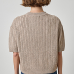 model wearing tan short sleeve sweater with jeans on a gray background.