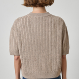 model wearing tan short sleeve sweater with jeans on a gray background.
