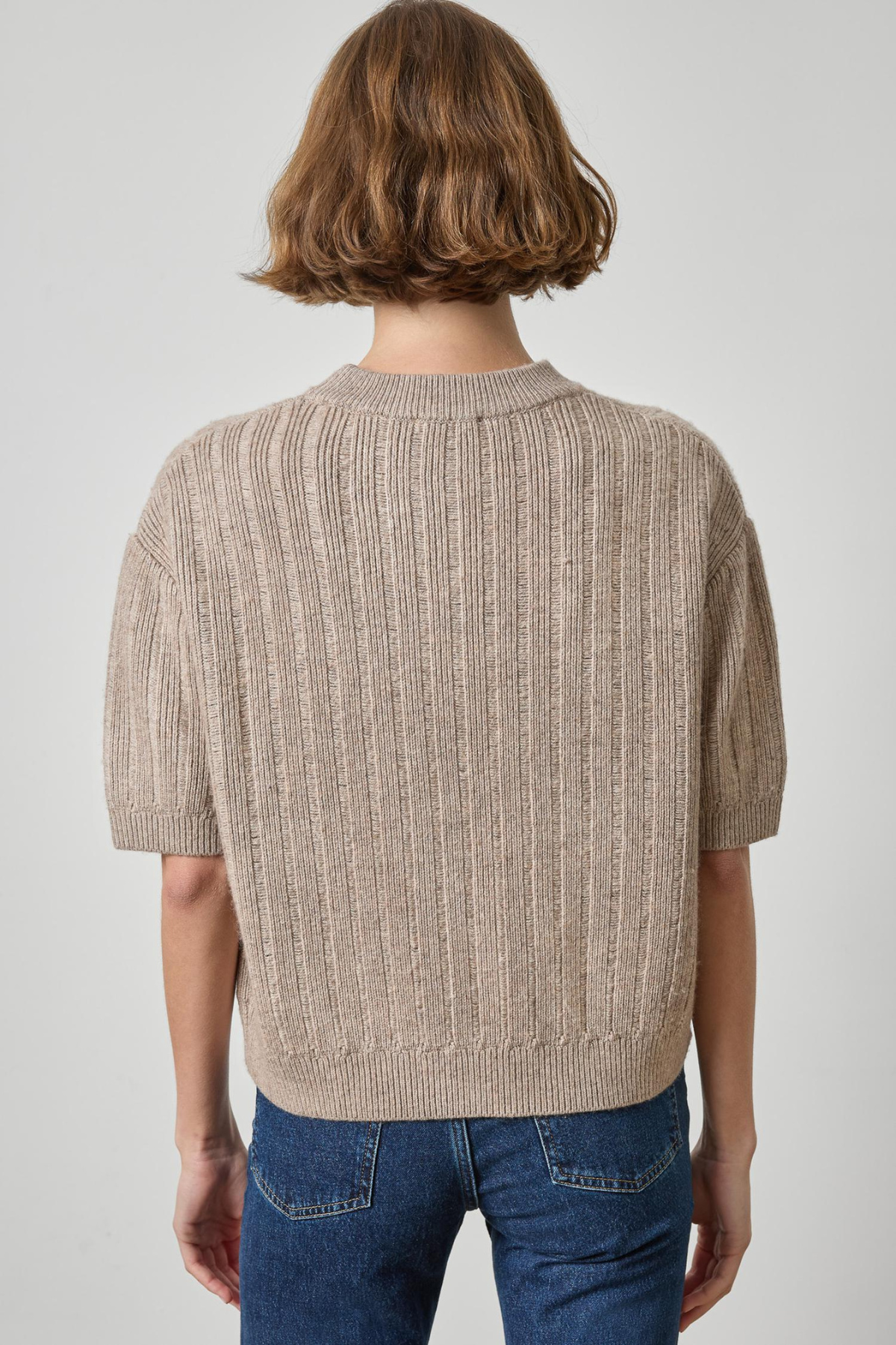 model wearing tan short sleeve sweater with jeans on a gray background.