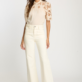 Woman wearing a beige floral blouse and white pants on a white background