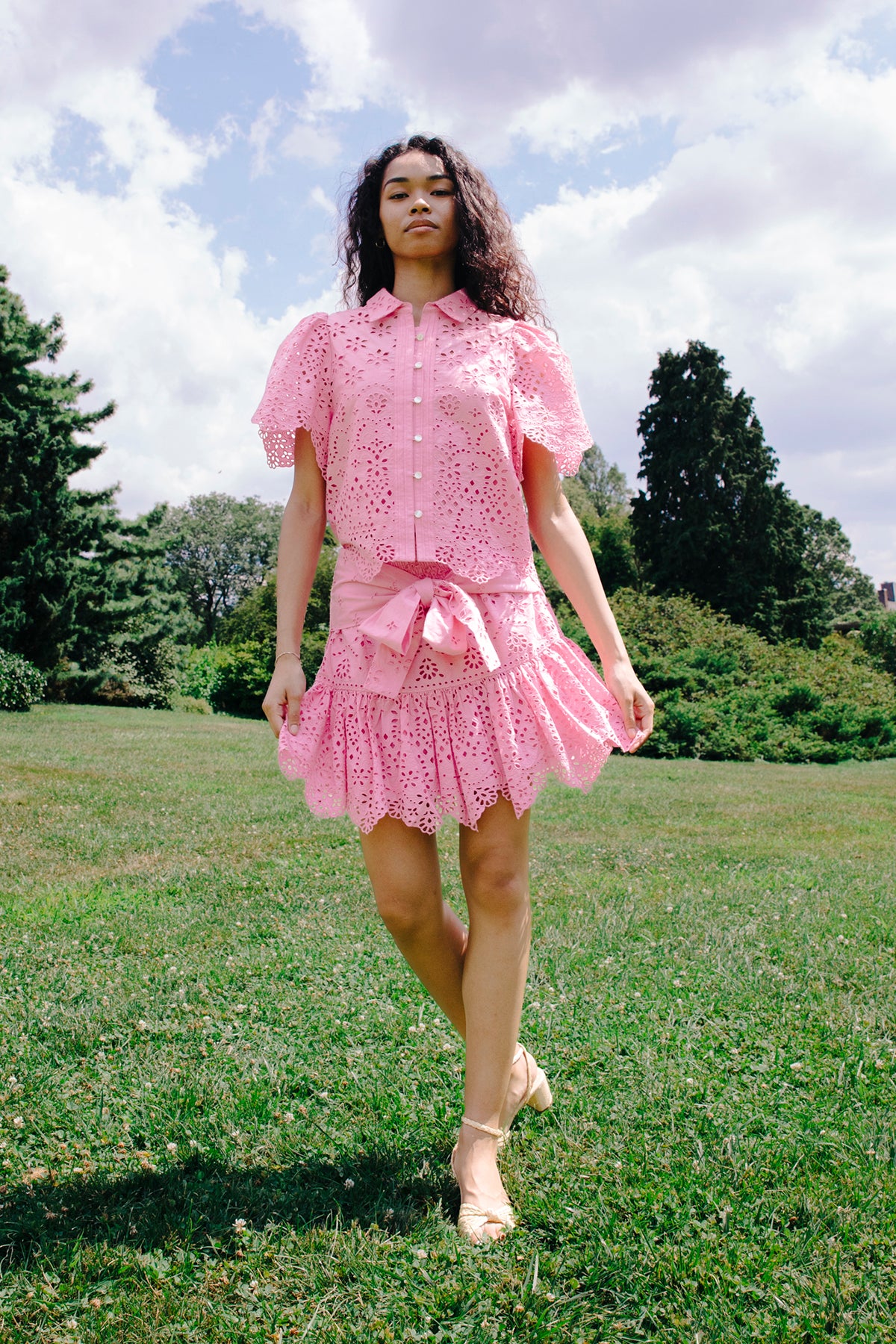 Woman in a pink outfit walking on grass with trees in the background