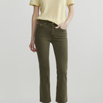 A model wearing a pale yellow short-sleeve knit top and olive green cropped jeans with dark brown pointed flats, standing against a light gray studio background.