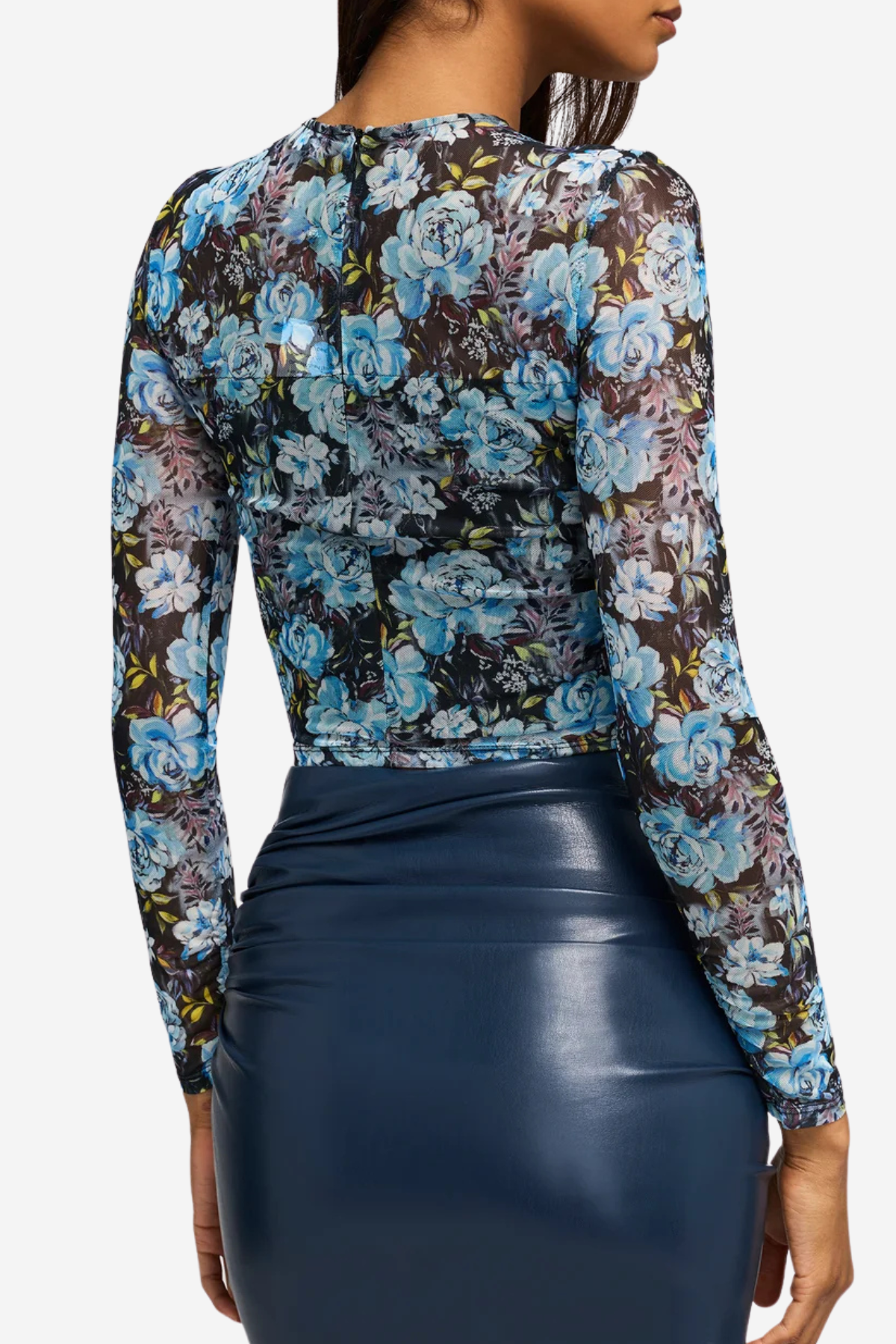 A woman shown from the back wearing a sheer long-sleeve floral mesh top with blue, purple, and black tones, paired with a dark navy faux-leather skirt, against a light gray studio background.