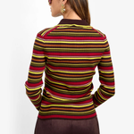 A woman shown from the back wearing a fitted long-sleeve knit sweater with horizontal stripes in red, yellow, and brown over a dark base, paired with dark brown pants against a plain light background.