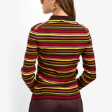 A woman shown from the back wearing a fitted long-sleeve knit sweater with horizontal stripes in red, yellow, and brown over a dark base, paired with dark brown pants against a plain light background.