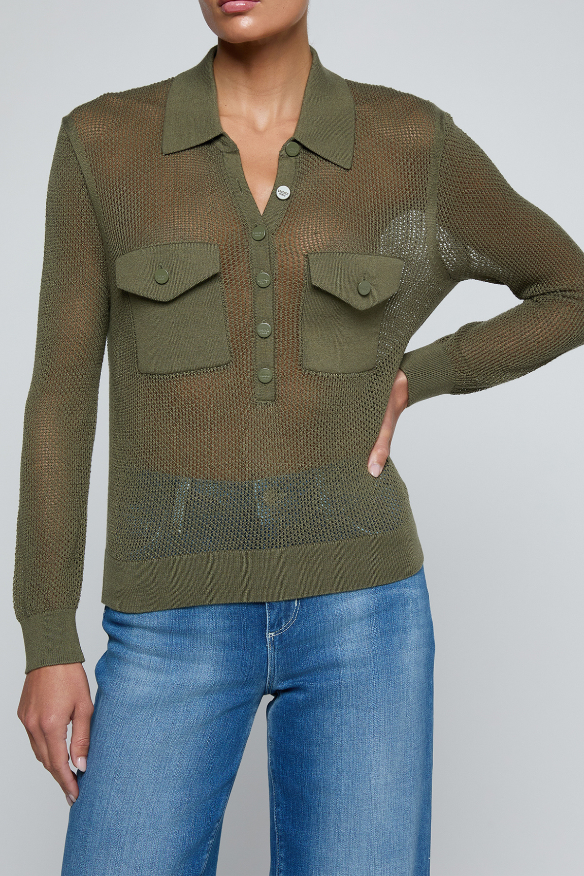 Model wearing a green knit button front sweater top with jeans on an off white background.