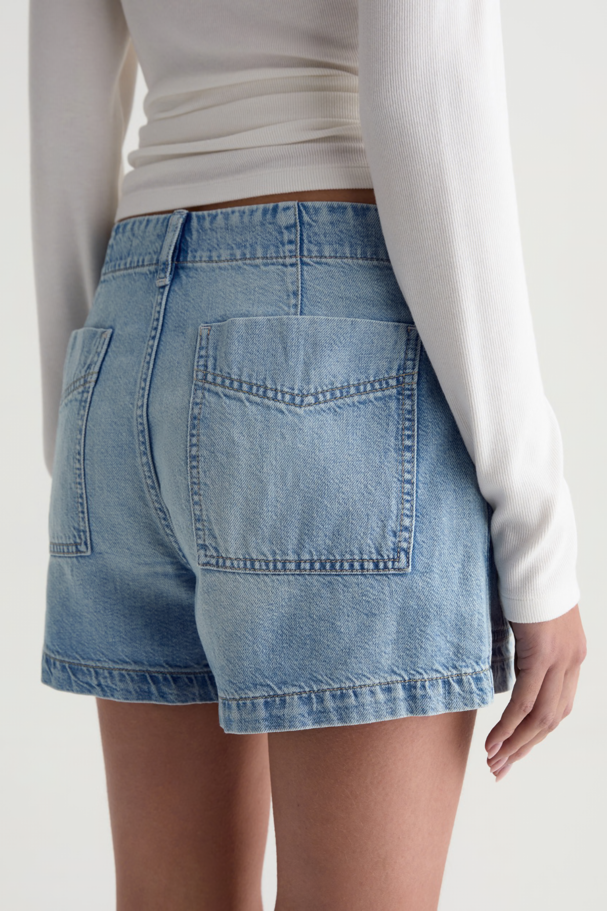 Person wearing light blue denim shorts on a plain background