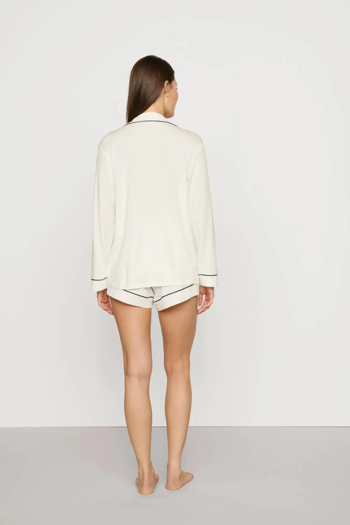 Person wearing a white long-sleeve shirt and shorts on a plain background
