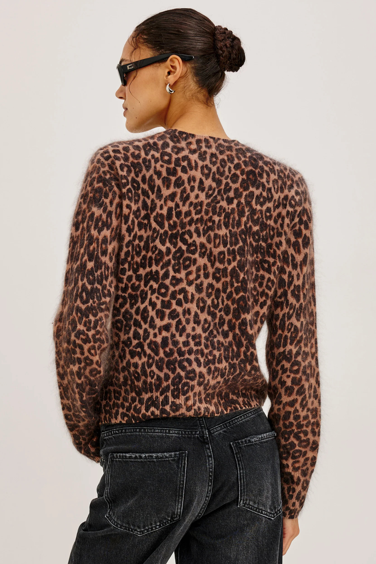 A woman shown from the back wearing a fuzzy leopard-print sweater and dark jeans against a plain light background.