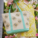 Woman holding a tote bag with eye designs and flowers in an outdoor setting