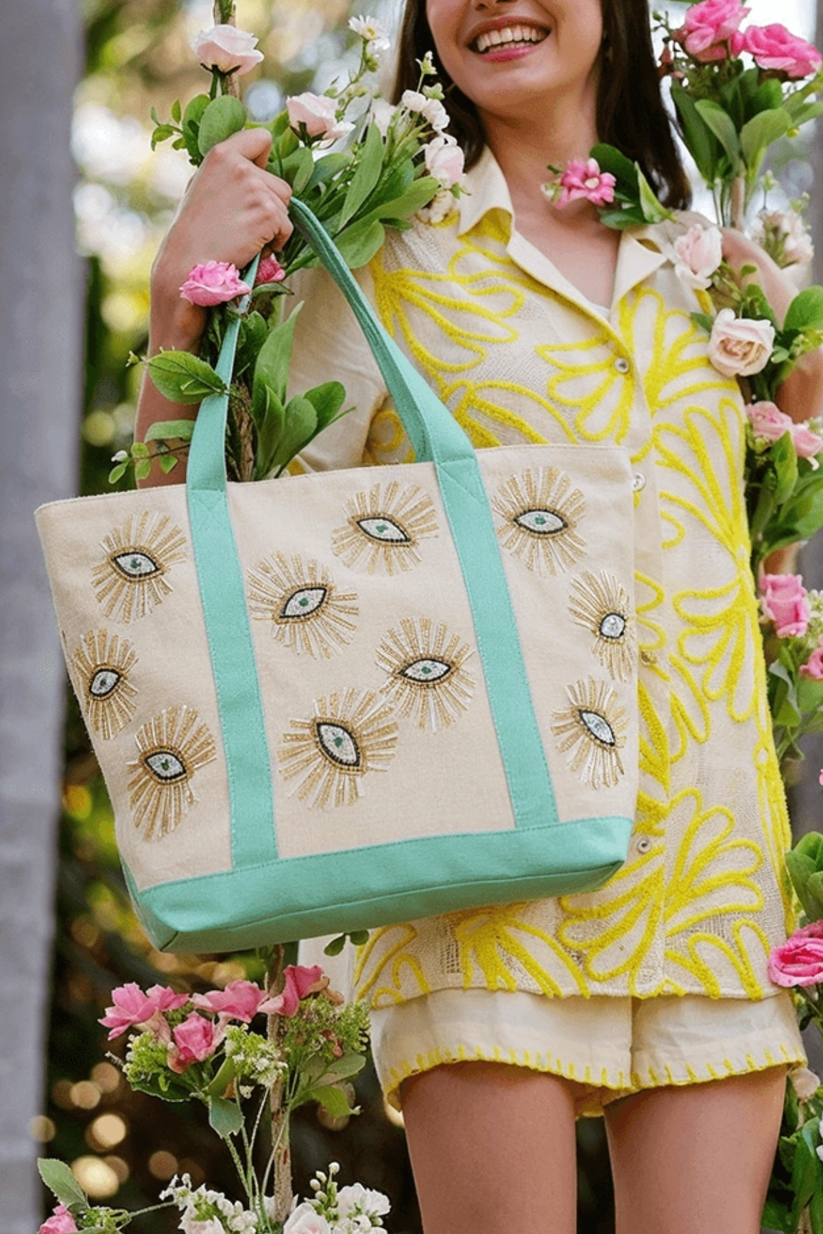 Woman holding a tote bag with eye designs and flowers in an outdoor setting