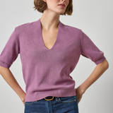 A woman modeling a short-sleeve V-neck knit sweater in dusty mauve purple, paired with blue jeans, against a light gray studio background.