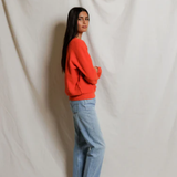 Person wearing a red sweater and blue jeans standing against a white draped curtain.