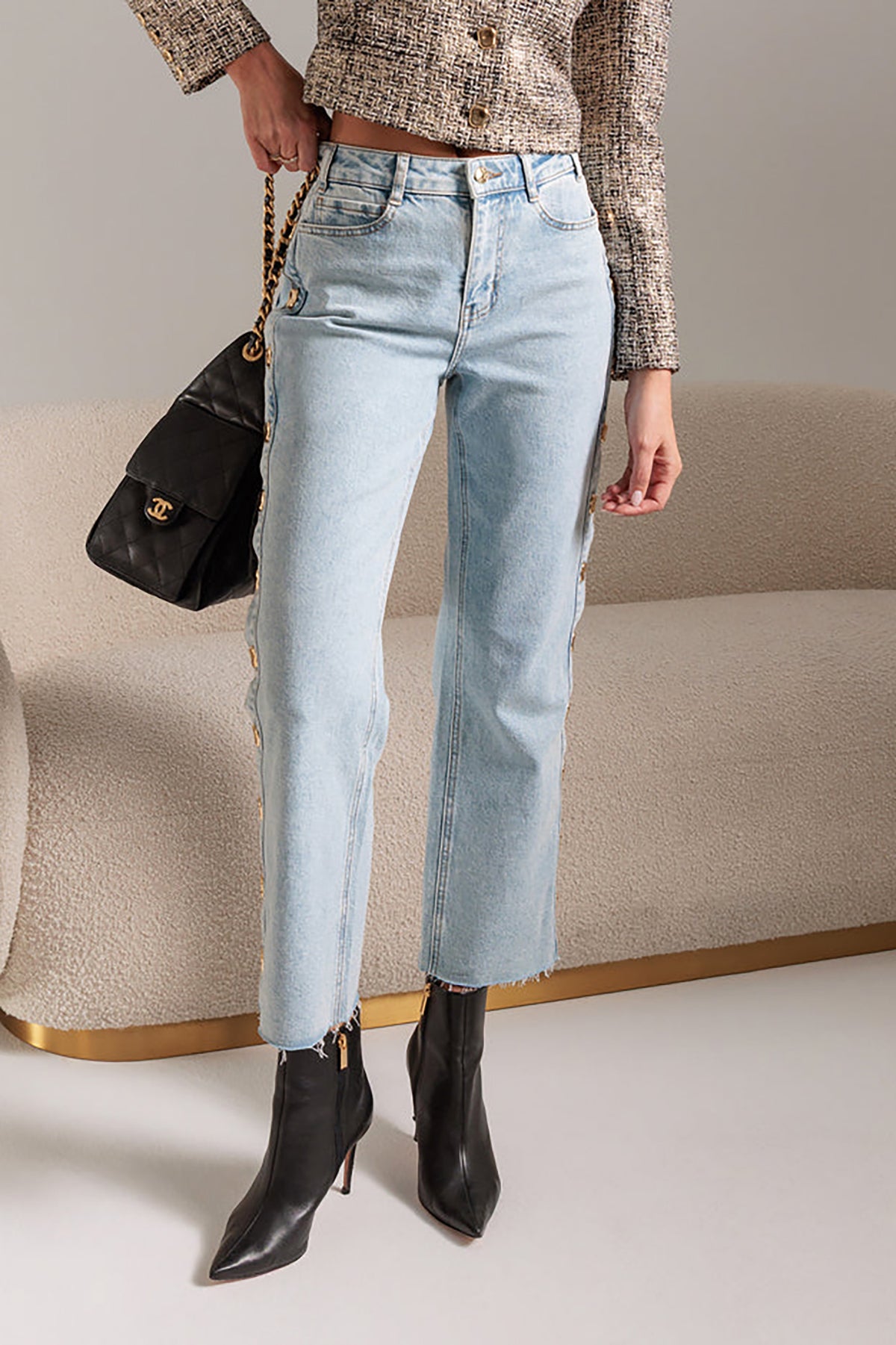 Person wearing light blue jeans and black ankle boots, holding a black handbag.