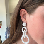 Model wearing white linked drop earrings with three open circular shapes in a contemporary statement silhouette.