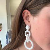 Model wearing white linked drop earrings with three open circular shapes in a contemporary statement silhouette.