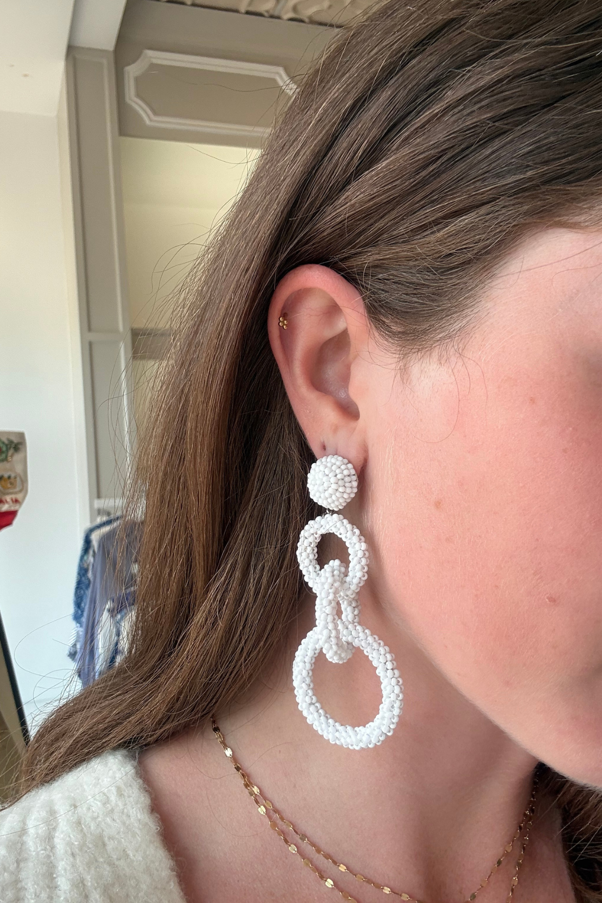 Model wearing white linked drop earrings with three open circular shapes in a contemporary statement silhouette.