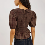 Woman wearing a brown plaid blouse and dark jeans on a plain background