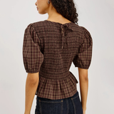 Woman wearing a brown plaid blouse and dark jeans on a plain background