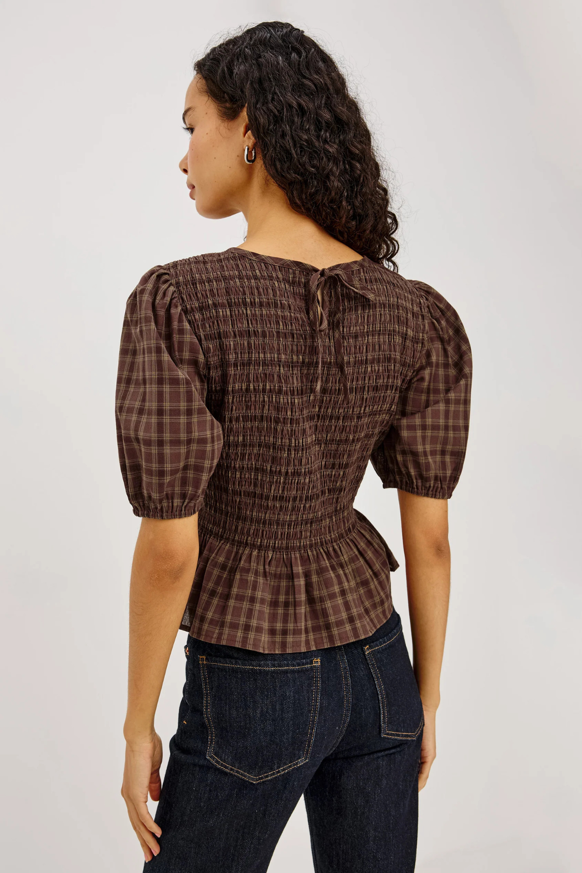 Woman wearing a brown plaid blouse and dark jeans on a plain background