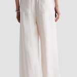 A person shown from the back wearing loose, wide-leg pants in a warm off-white or cream color, with an elastic waistband and two large patch pockets, against a light gray studio background.