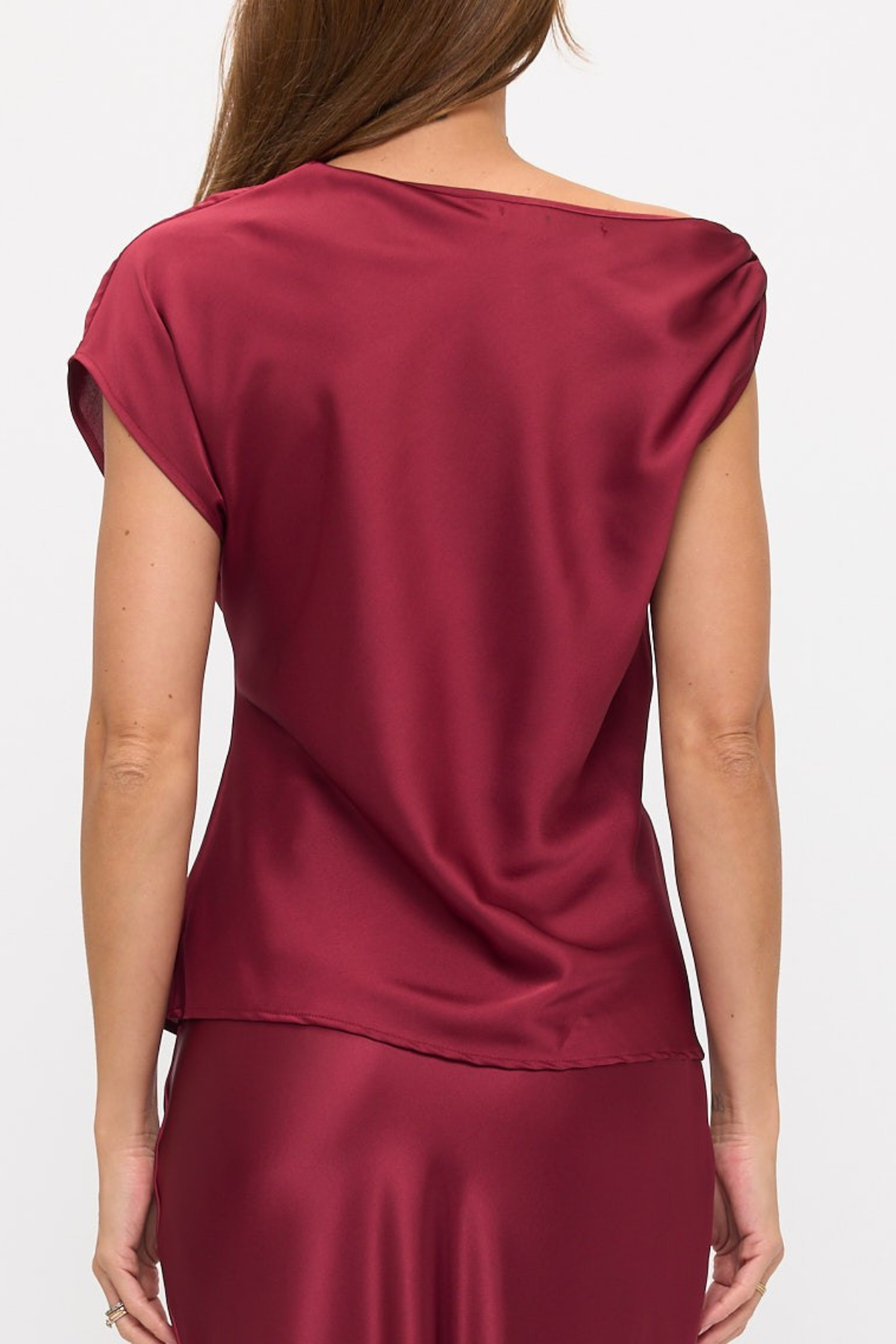 A woman shown from the back wearing a satin-like burgundy top with cap sleeves and a matching skirt against a plain light background.