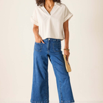 Woman wearing a white blouse and blue jeans against a plain background