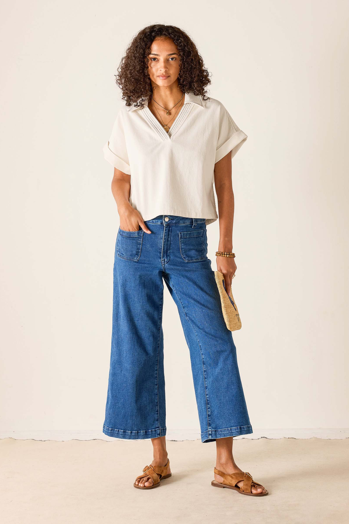 Woman wearing a white blouse and blue jeans against a plain background