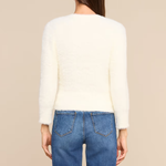 A woman shown from the back wearing a cream-colored, long-sleeve fuzzy knit top and blue jeans against a solid beige background.