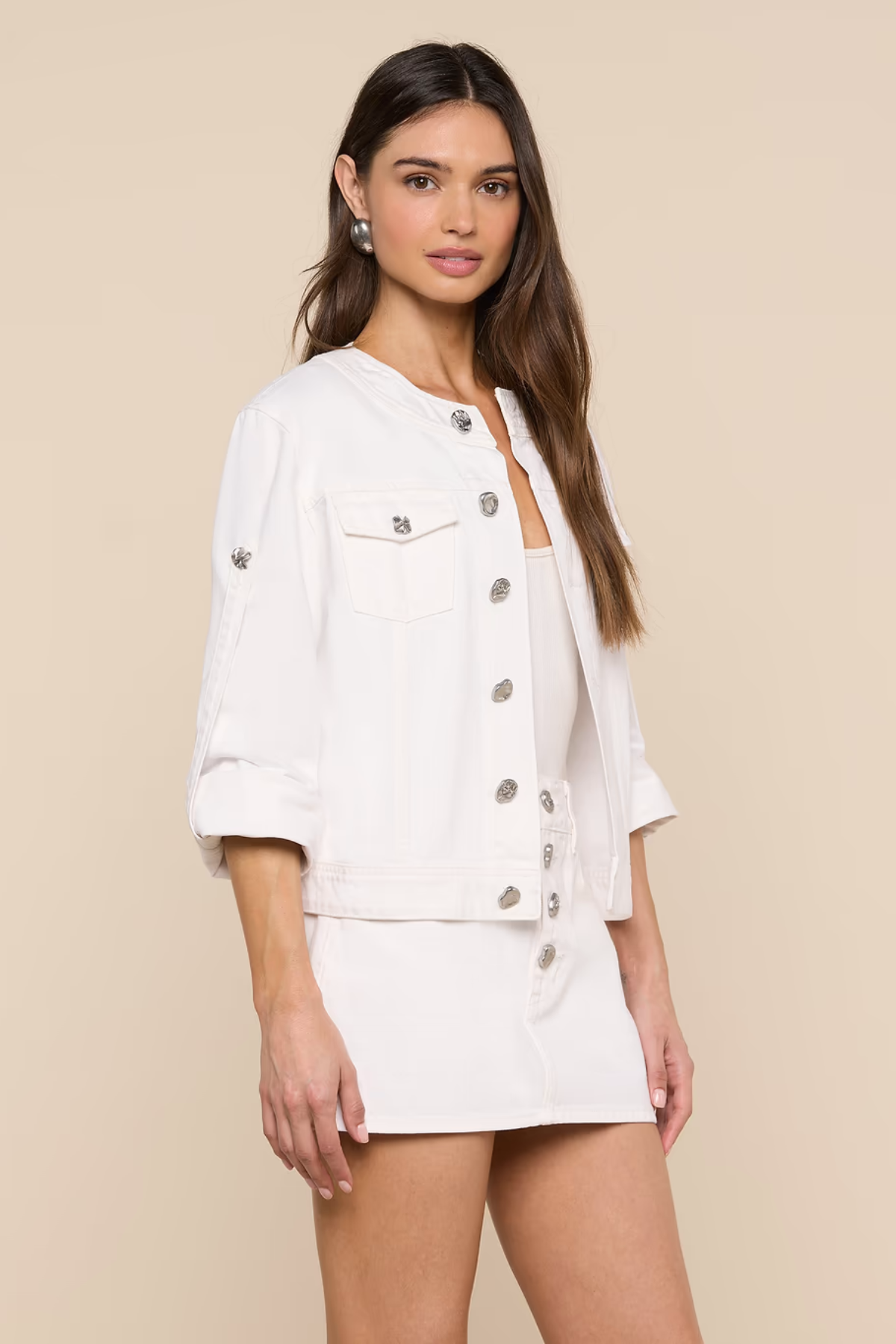 Woman wearing a white button-up jacket and skirt set against a beige background