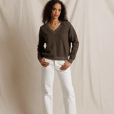 Woman wearing a brown sweater and white pants against a plain background