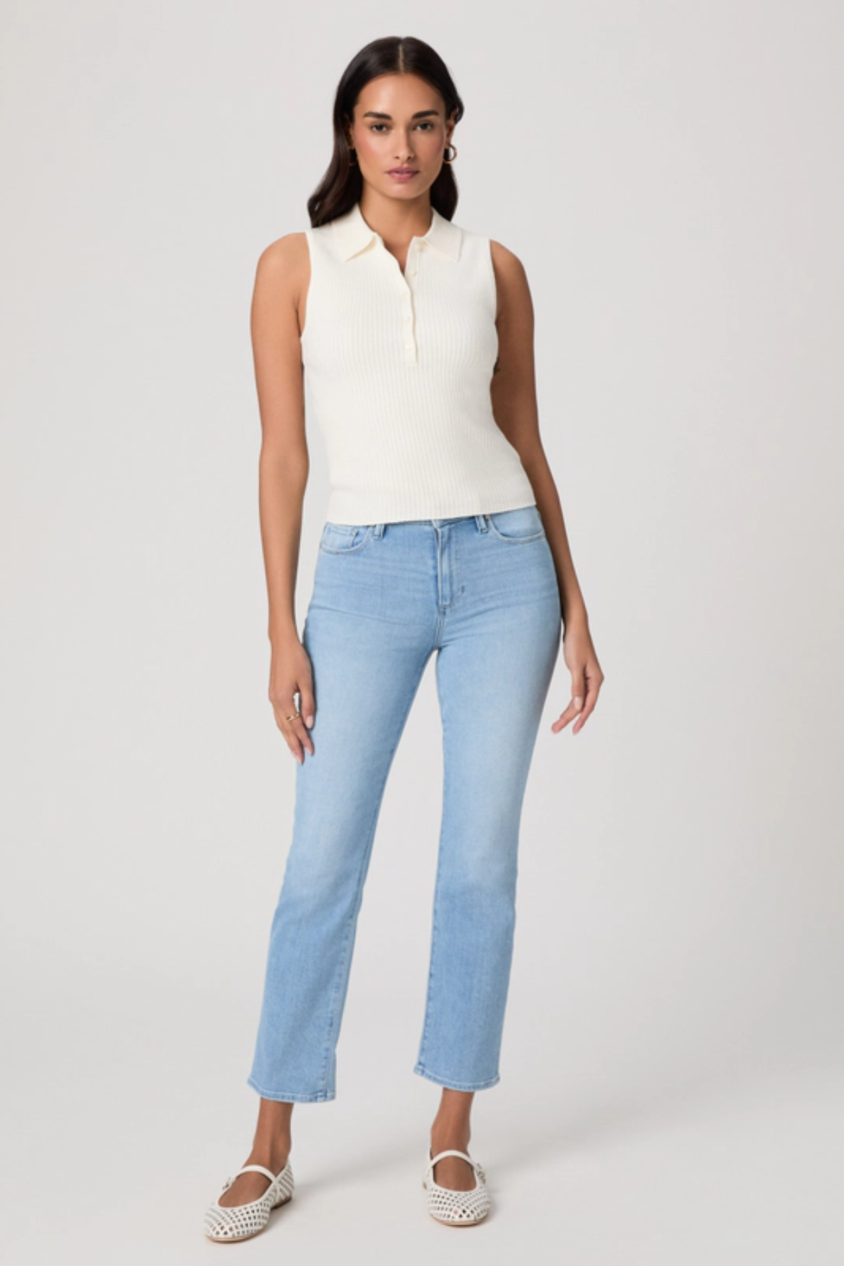 Woman wearing a white sleeveless top and light blue jeans on a white background
