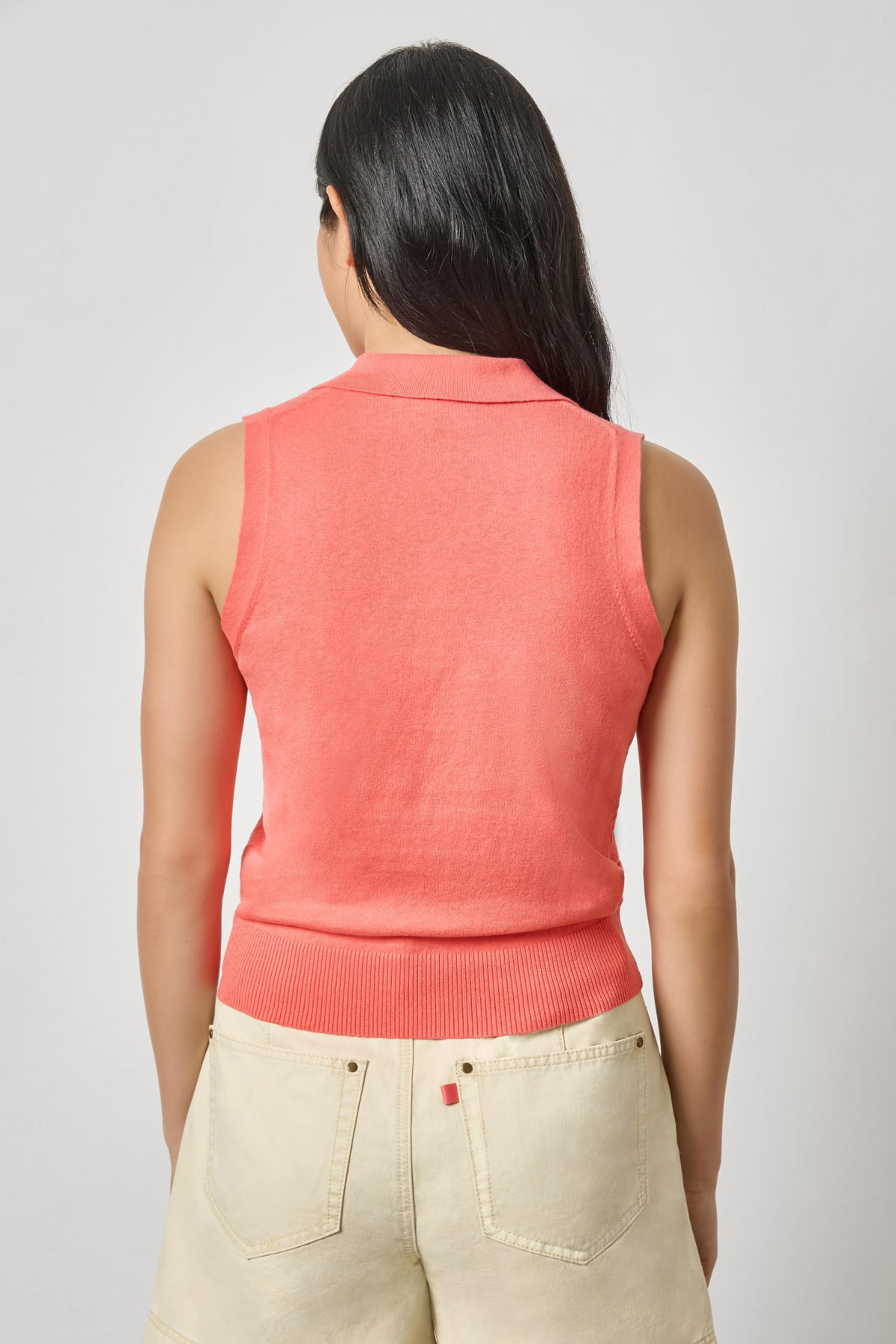 Person wearing a coral sleeveless top and beige pants on a light gray background
