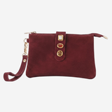 A burgundy suede wristlet clutch with gold-tone hardware, featuring a front strap closure with three decorative gold-tone buttons and a matching wristlet strap, shown against a plain light gray background.