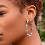 Close-up of a person wearing turquoise beaded hoop earrings with a blurred natural background