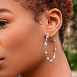 Close-up of a person wearing turquoise beaded hoop earrings with a blurred natural background