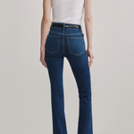 A model shown from the back wearing dark blue high-waisted flare jeans, a white sleeveless top, and brown heels against a light gray studio background.