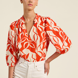 Woman wearing a red and white patterned blouse with white pants on a beige background